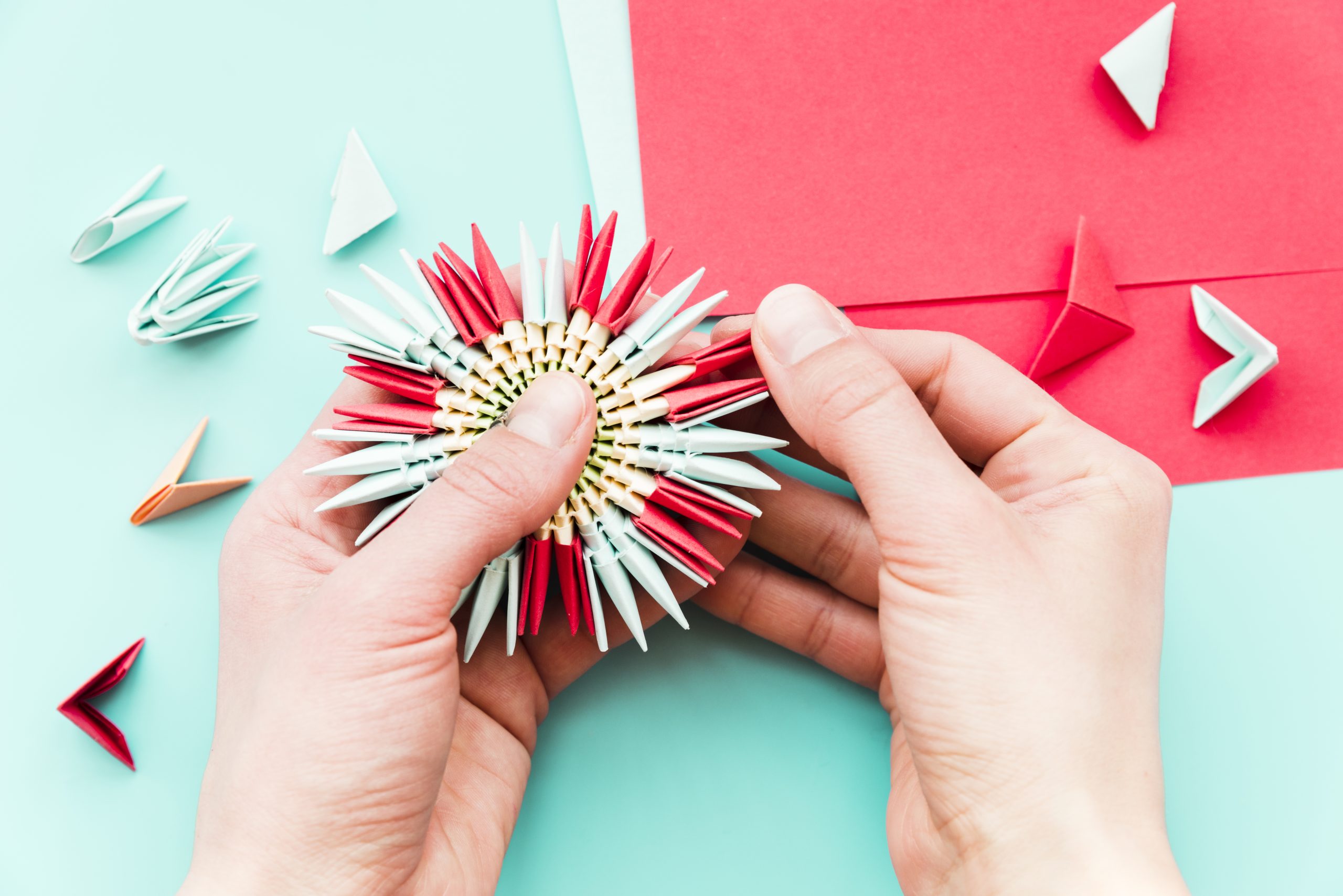 close up person s hand making paper flower teal background